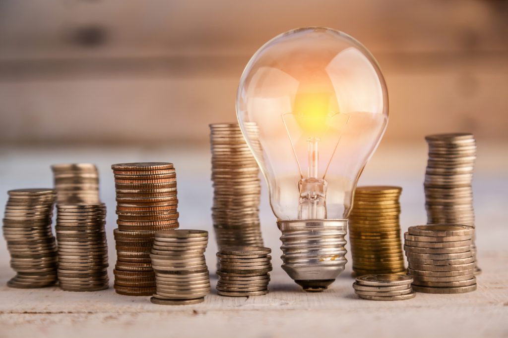 Glowing lightbulb tilted against stacks of coins.