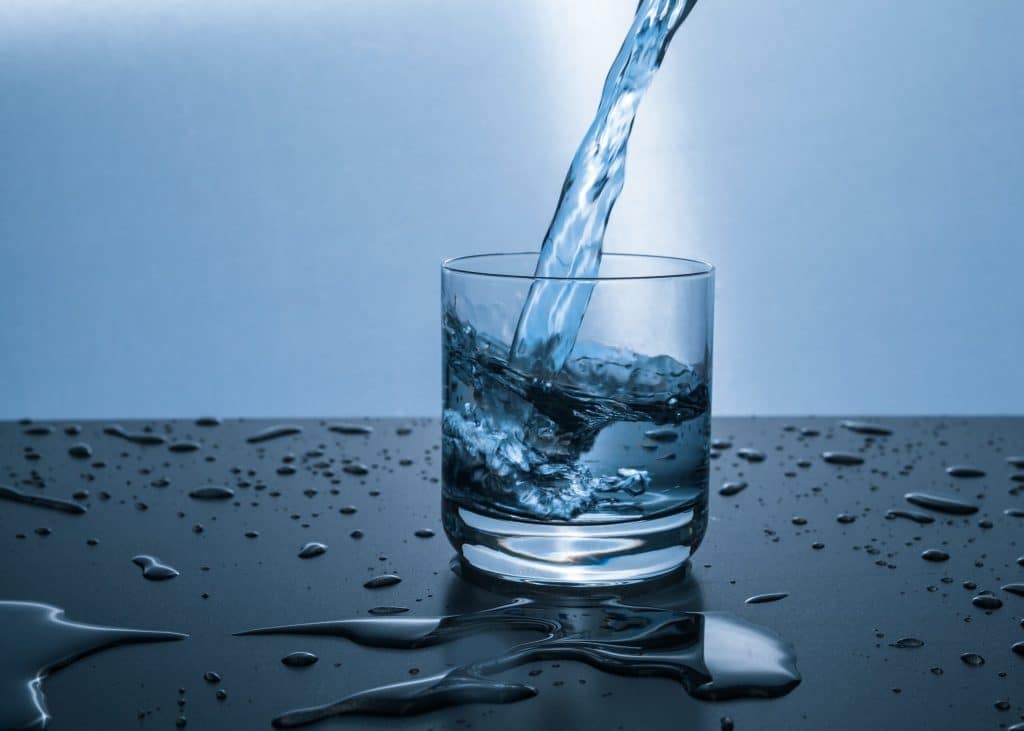 A glass cup sets on a counter as water is poured into it from above.